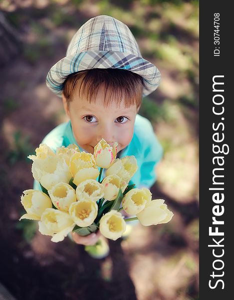 On the nature of the little boy in a blue shirt with a bouquet of white tulips. On the nature of the little boy in a blue shirt with a bouquet of white tulips