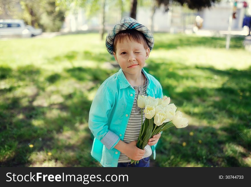 On the nature of the little boy in a blue shirt with a bouquet of white tulips. On the nature of the little boy in a blue shirt with a bouquet of white tulips