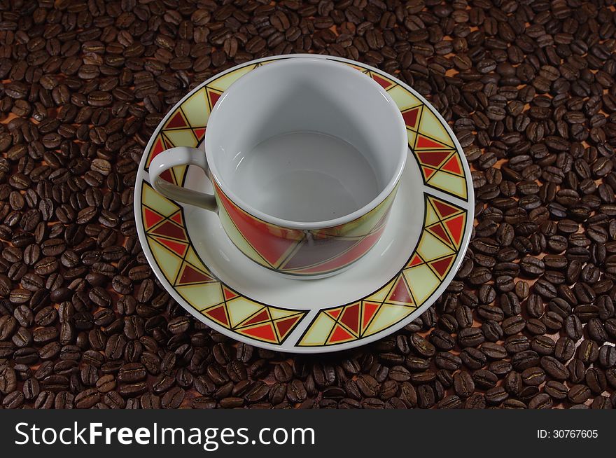 The photograph shows a porcelain cup on a saucer on the background of coffee beans. The photograph shows a porcelain cup on a saucer on the background of coffee beans.