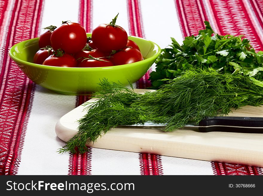 On a cutting board dill, parsley and ripe tomatoes in green bowl