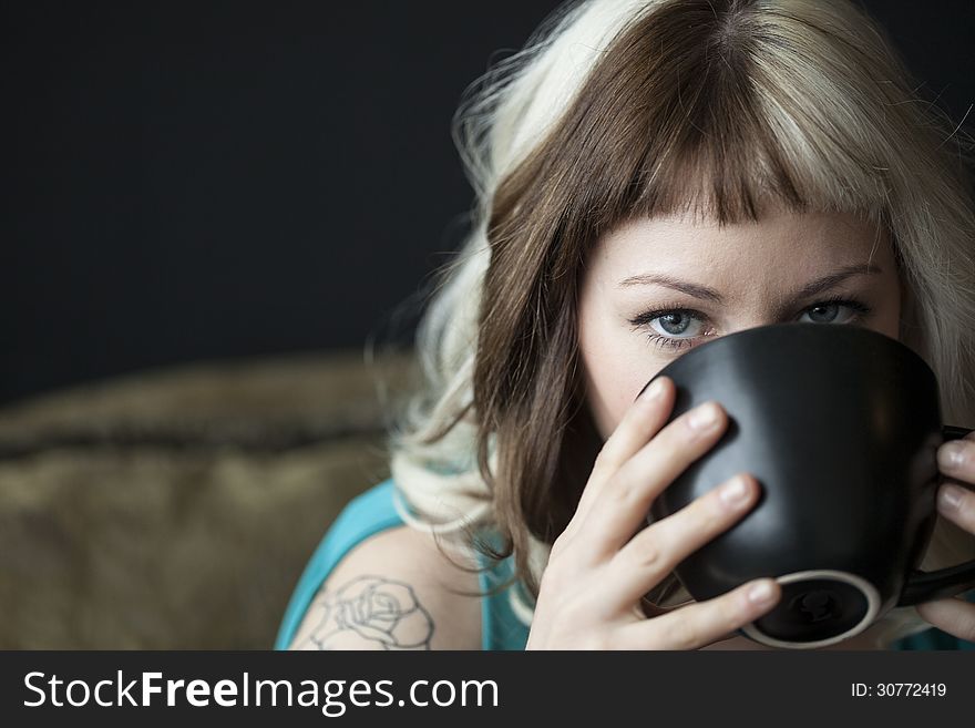 Portrait of a beautiful young woman with brown and blond hair looking right into the camera. She is also holding a black coffee cup and wearing a blue dress. Portrait of a beautiful young woman with brown and blond hair looking right into the camera. She is also holding a black coffee cup and wearing a blue dress.