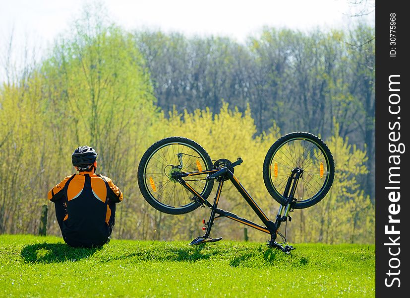 Cyclist Sitting on the Spring Grass Near His Bike