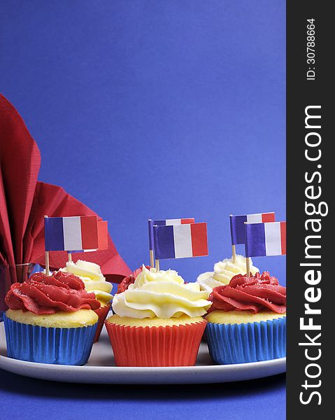 French theme red, white and blue mini cupcake cakes with flags of France and fleur-de-lis red napkin for National holidays of France, Bastille Day, the Fourteenth of July. Vertical with copy space for your text here. French theme red, white and blue mini cupcake cakes with flags of France and fleur-de-lis red napkin for National holidays of France, Bastille Day, the Fourteenth of July. Vertical with copy space for your text here.