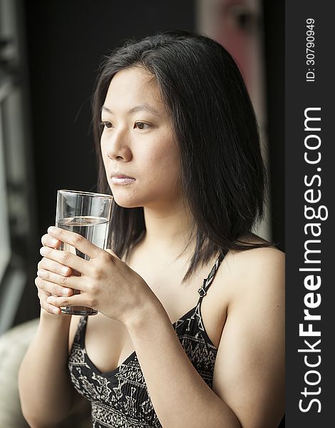 Beautiful Asian woman with brown hair and eyes drinking water from a glass. Beautiful Asian woman with brown hair and eyes drinking water from a glass.