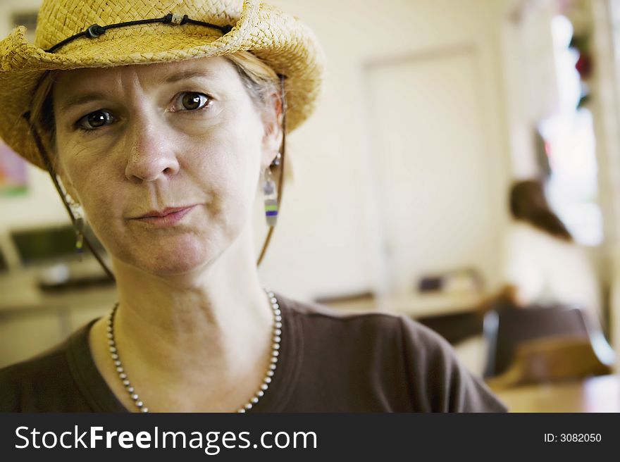Woman indoors in a cowboy hat looks intently at the camera. Woman indoors in a cowboy hat looks intently at the camera.