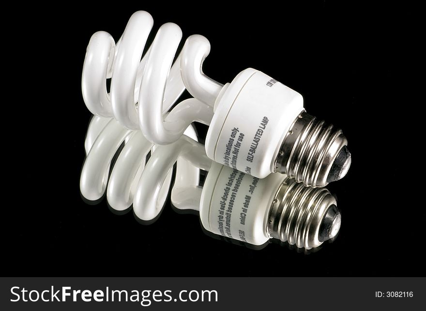 An energy effecient fluorescent light bulb isolated on a black background, shot over a mirror. An energy effecient fluorescent light bulb isolated on a black background, shot over a mirror