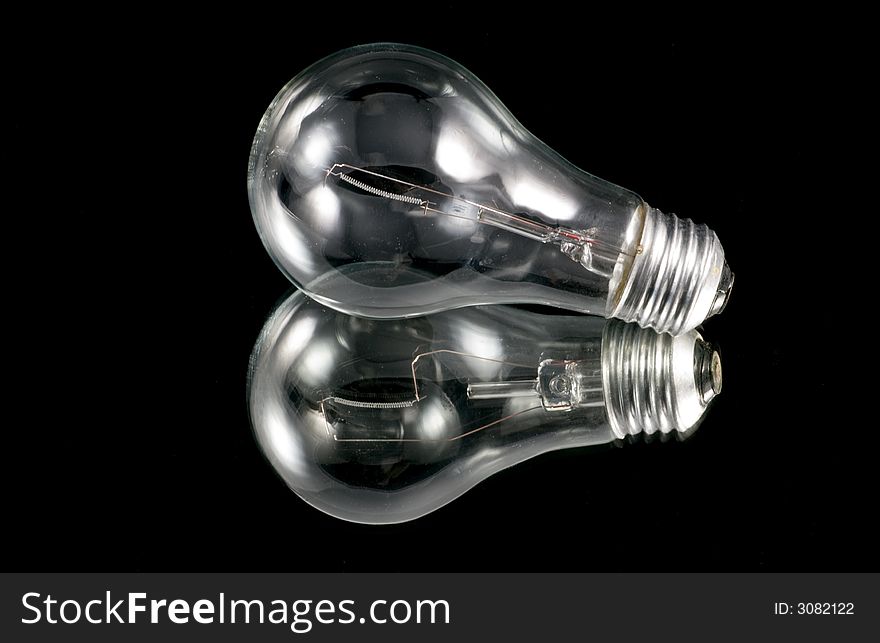 An old incandescent light bulb on black background over a mirror