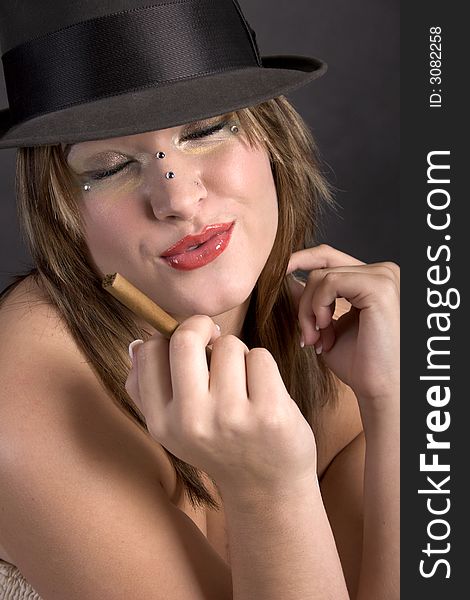 Pretty young woman in a man's hat with an unlit cigar in her hand. Pretty young woman in a man's hat with an unlit cigar in her hand