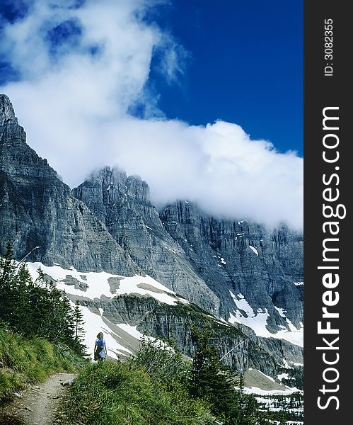 Female Hiker on mountain trail with dramatic peaks and swirling clouds against dark blue sky. Female Hiker on mountain trail with dramatic peaks and swirling clouds against dark blue sky