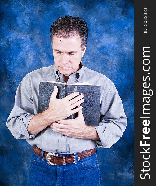 A man standing and tenderly holding an old bible to his chest. A man standing and tenderly holding an old bible to his chest.