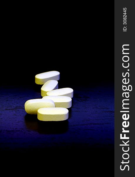 Some white/yellow/cream colored pills/vitamins on a black and blue background. Some white/yellow/cream colored pills/vitamins on a black and blue background.