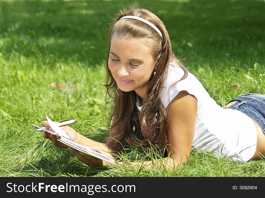 Beautiful young girl reading notes on the grass