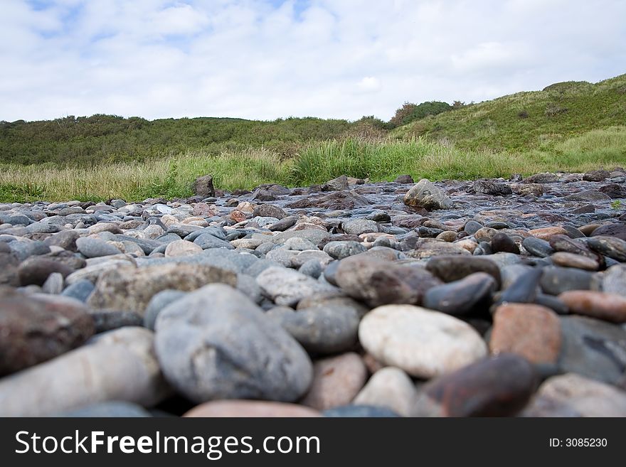 Pebbles on a beach in front of a grass bank