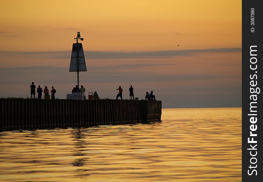 Several people gather on the end of the pier to watch the sun go down over the lake. Several people gather on the end of the pier to watch the sun go down over the lake.