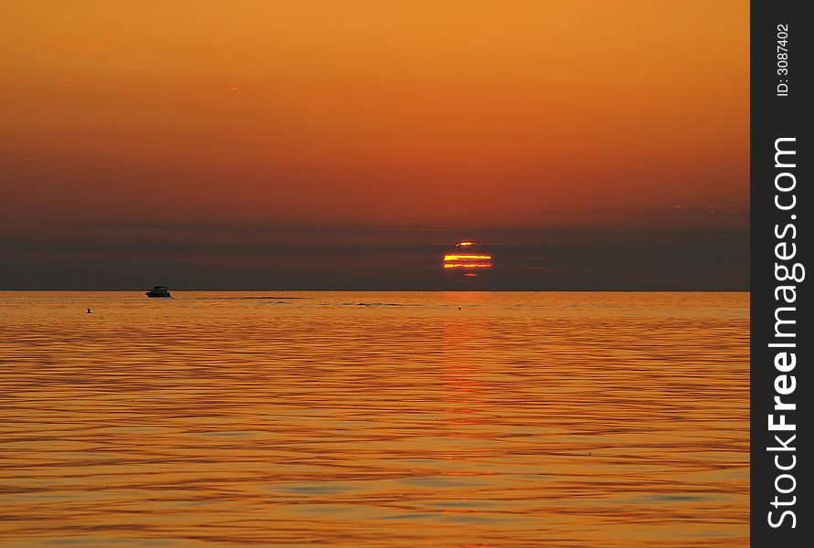 The sun glimpsed through clouds just as it sets over still water. The sun glimpsed through clouds just as it sets over still water.