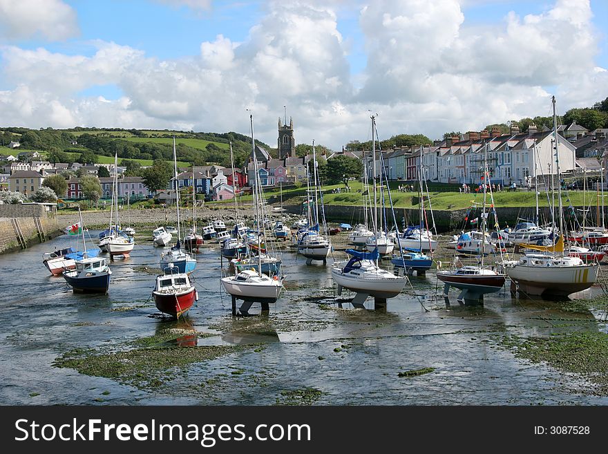 Sailing boats at anchor in a small harbour with the tide out and colorful houses to the rear. Location Aberaeron, Wales, United Kingdom.