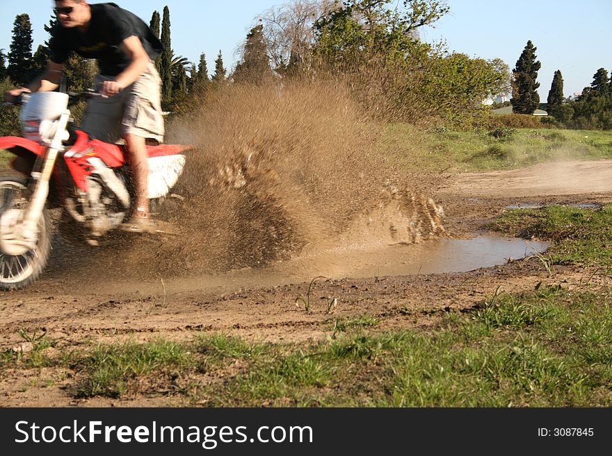 Young biker riding through a pool of mud. Young biker riding through a pool of mud