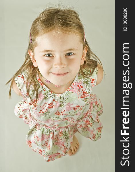 Bird's eye portrait of a smiling young girl in a print dress. Plain background, isolated, vertical.