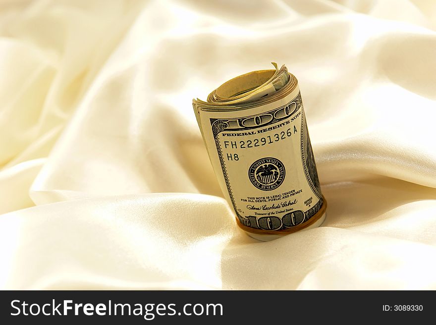 Close up of roll of hundred dollar bills with rubber band on satin background. Close up of roll of hundred dollar bills with rubber band on satin background