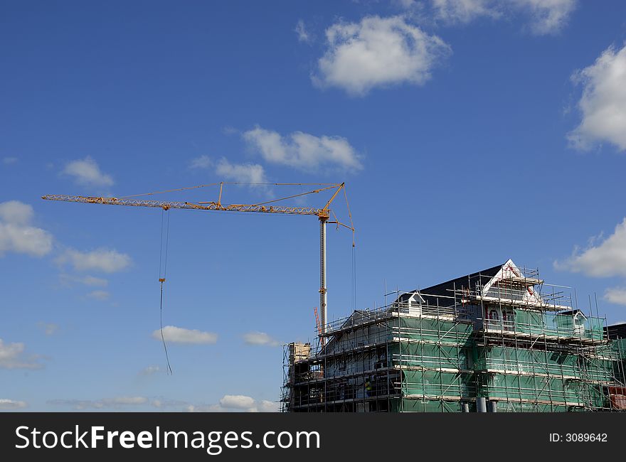 Tall crane against a blue sky with a construction site surrounded with scaffolding and plenty of copy space. Tall crane against a blue sky with a construction site surrounded with scaffolding and plenty of copy space