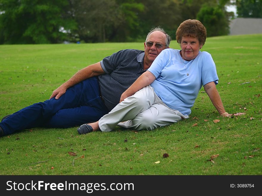 Senior couple laying outside on a grass hill