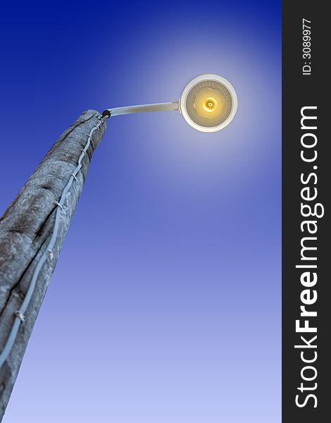 A brightly lit street lamp against a blue sky