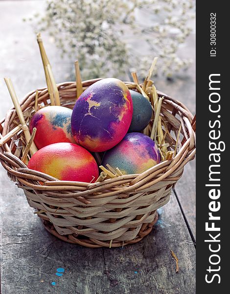 Colored easter eggs in basket on wooden table