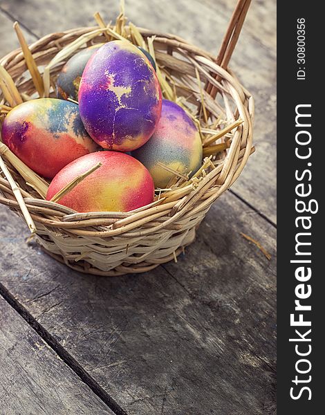 Colored easter eggs in basket on wooden table