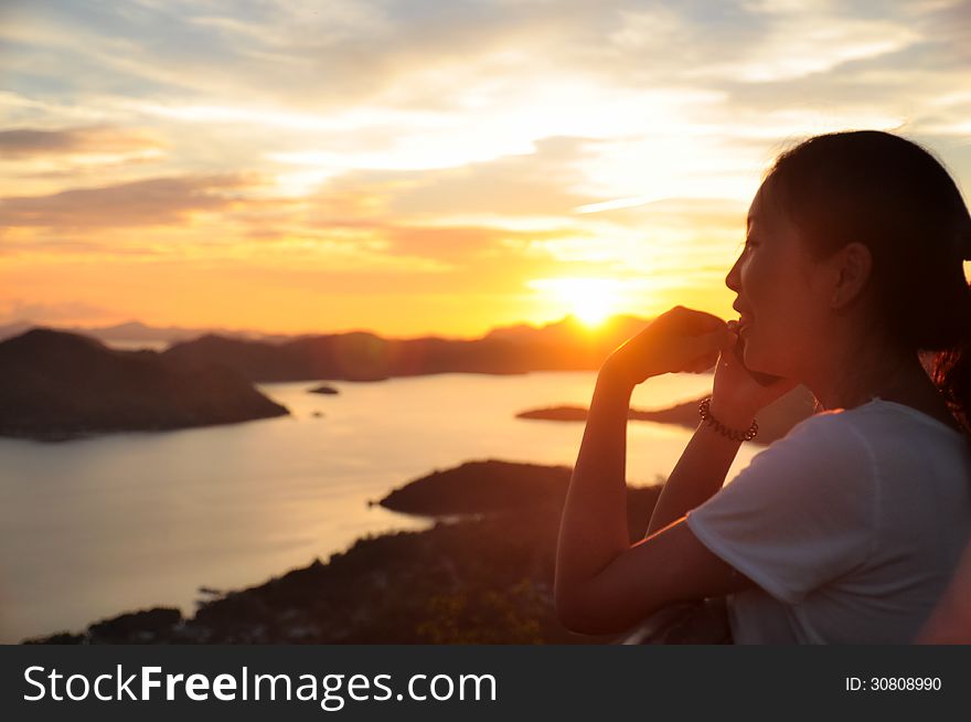 Young girl talks to family on the phone on Chinese New Year with background of beautiful sunset over ocean. Shot on Coron town, Palawan, Philippines. Young girl talks to family on the phone on Chinese New Year with background of beautiful sunset over ocean. Shot on Coron town, Palawan, Philippines
