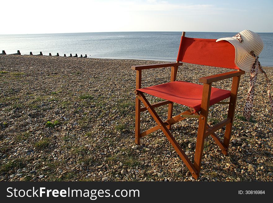 Folding wooden chair on the beach with a straw hat