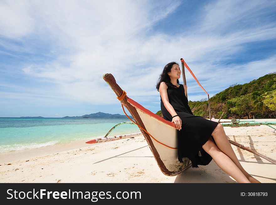 Portrait of happy young girl in black long skirt sitting on a banca (a type of outrigger boat native to the Philippines) on white beach. Shot on Malcapuya Island, Coron, Philippines. Portrait of happy young girl in black long skirt sitting on a banca (a type of outrigger boat native to the Philippines) on white beach. Shot on Malcapuya Island, Coron, Philippines