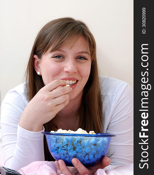 Beautiful young woman enjoying eating popcorn and talking on cell phone on her bed. Beautiful young woman enjoying eating popcorn and talking on cell phone on her bed.