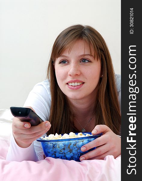 Beautiful young woman enjoying eating popcorn and holding tv control. Beautiful young woman enjoying eating popcorn and holding tv control.