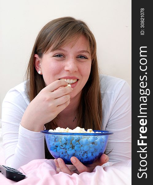 Beautiful young woman enjoying eating popcorn and talking on cell phone on her bed. Beautiful young woman enjoying eating popcorn and talking on cell phone on her bed