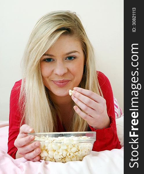 Young blonde woman eating popcorn on bed. Young blonde woman eating popcorn on bed