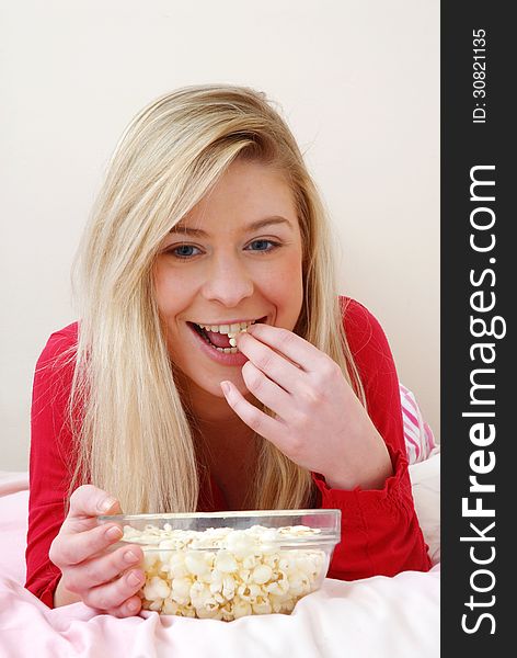 Young blonde woman eating popcorn on bed. Young blonde woman eating popcorn on bed