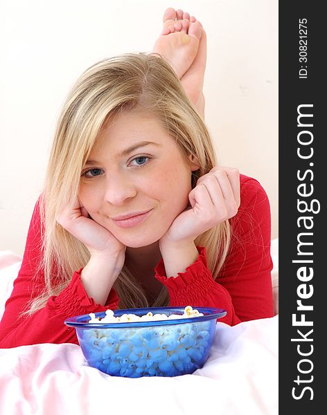 Beautiful young blonde woman enjoying eating popcorn on her bed. Beautiful young blonde woman enjoying eating popcorn on her bed.