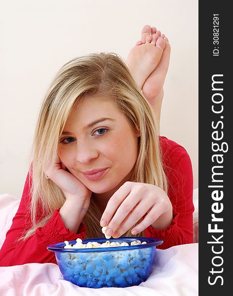 Beautiful young blonde woman enjoying eating popcorn on her bed. Beautiful young blonde woman enjoying eating popcorn on her bed.