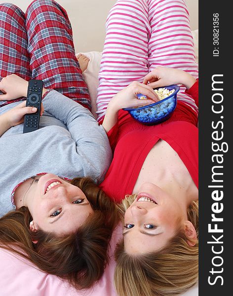 Two young women eating popcorn on bed. Two young women eating popcorn on bed