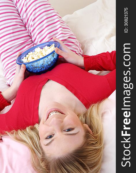 Beautiful young blonde woman enjoying eating popcorn on her bed. Beautiful young blonde woman enjoying eating popcorn on her bed