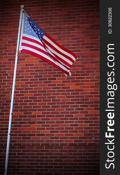 An American flag on a pole flying against a red brick wall. An American flag on a pole flying against a red brick wall.