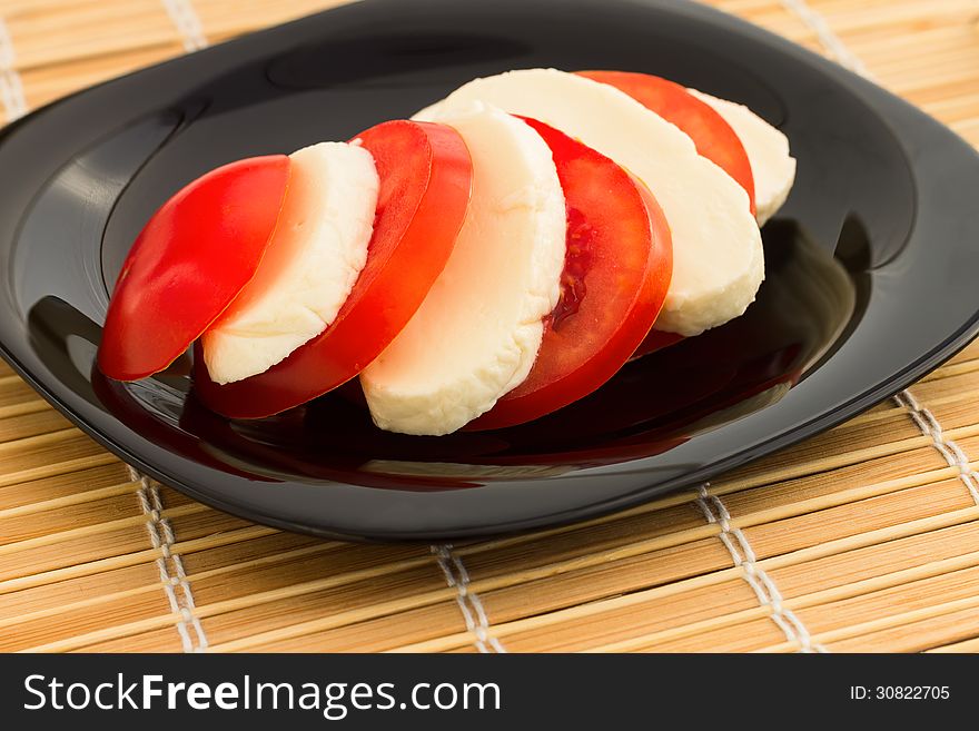 Tomato and mozzarella on black dish at bamboo background