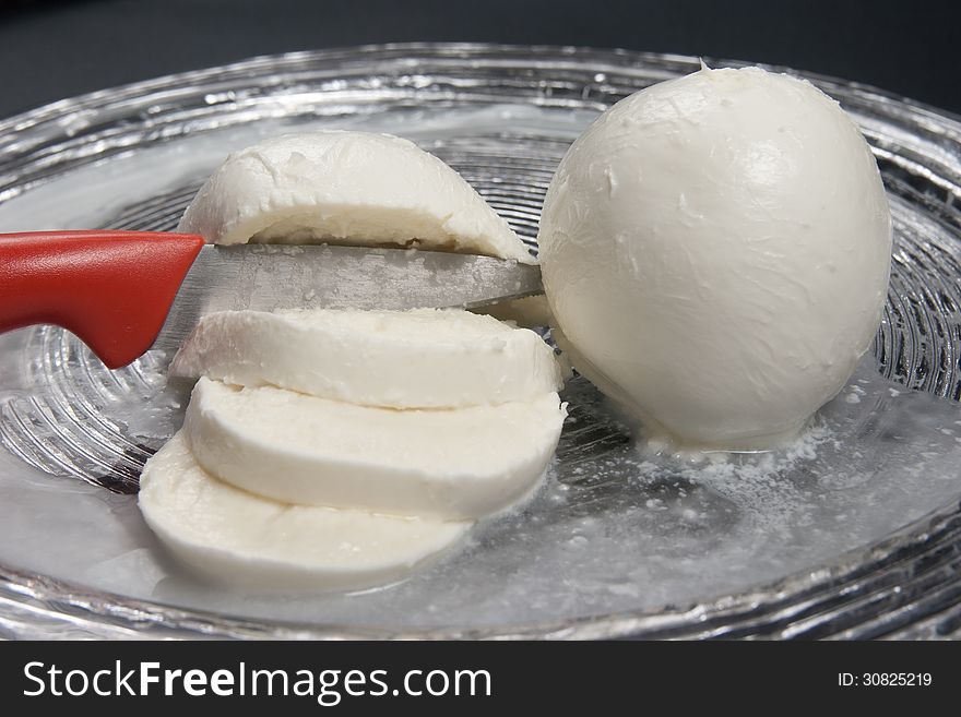 Typical fresh Italian cheese made ??with buffalo or cow milk in glass dish on a black background. Typical fresh Italian cheese made ??with buffalo or cow milk in glass dish on a black background