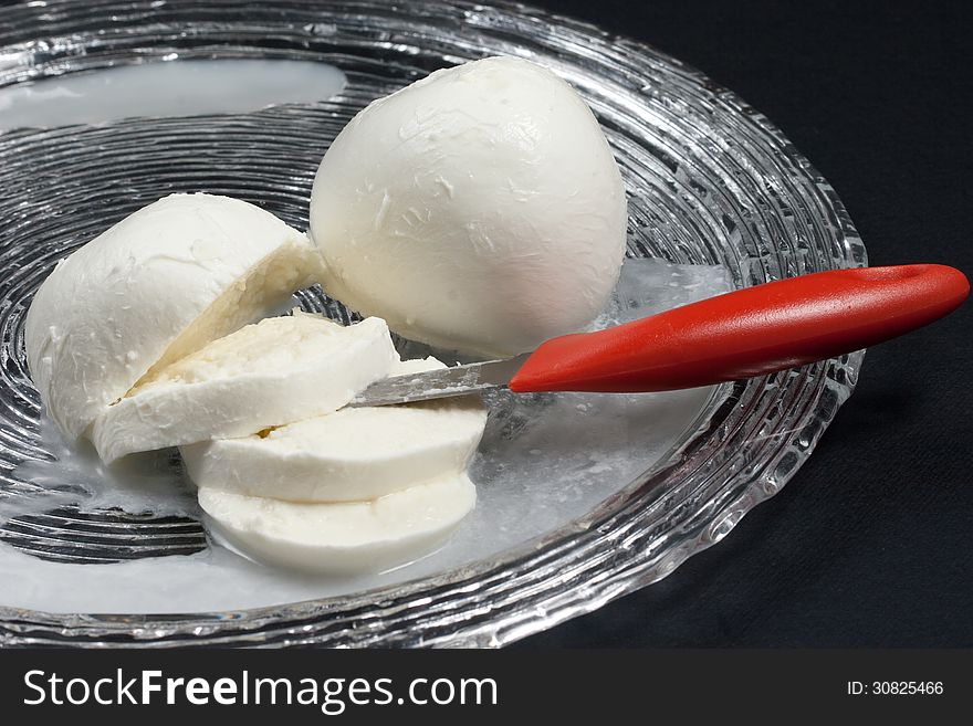 Typical fresh Italian cheese made ??with buffalo or cow milk in glass dish on a black background. Typical fresh Italian cheese made ??with buffalo or cow milk in glass dish on a black background