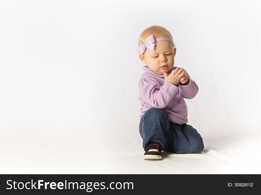 A baby girl kneels and inspects her hand. A baby girl kneels and inspects her hand