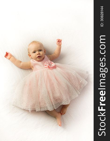 A serene little girl dressed in a pink frilly dress lays on a white background. A serene little girl dressed in a pink frilly dress lays on a white background