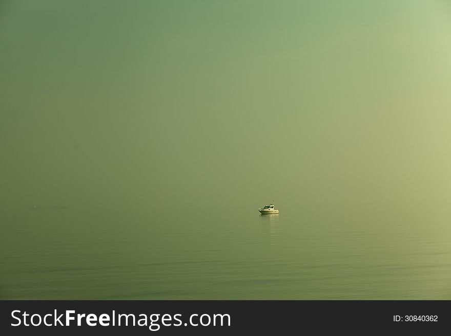 A motorboat lost in a green sea, with the mist that mixes water and sky.