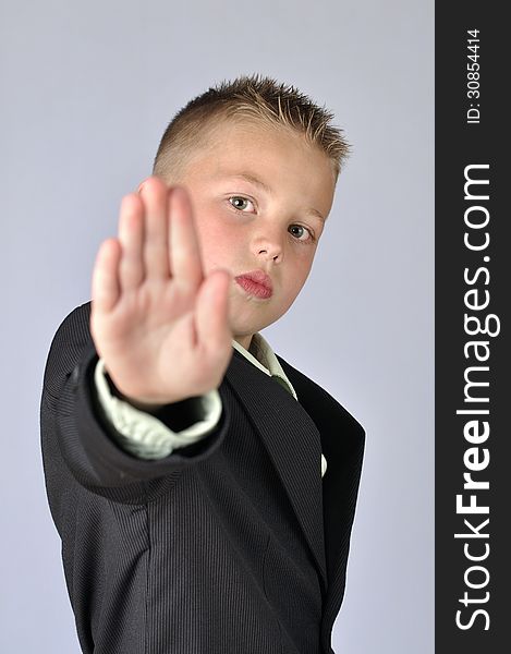 Young child in business suit with hand extended out to say stop on gray background. Young child in business suit with hand extended out to say stop on gray background