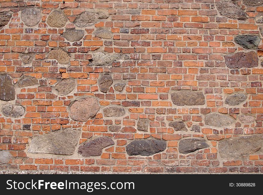 The photograph shows a wall, which is a fragment of an old church. It is made of bricks and large boulders of stone. The photograph shows a wall, which is a fragment of an old church. It is made of bricks and large boulders of stone.