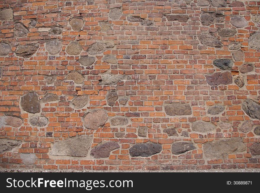 The photograph shows a wall, which is a fragment of an old church. It is made of bricks and large boulders of stone. The photograph shows a wall, which is a fragment of an old church. It is made of bricks and large boulders of stone.